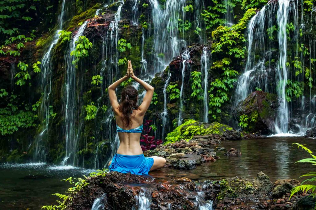 Woman doing yoga in the forest by a waterfall